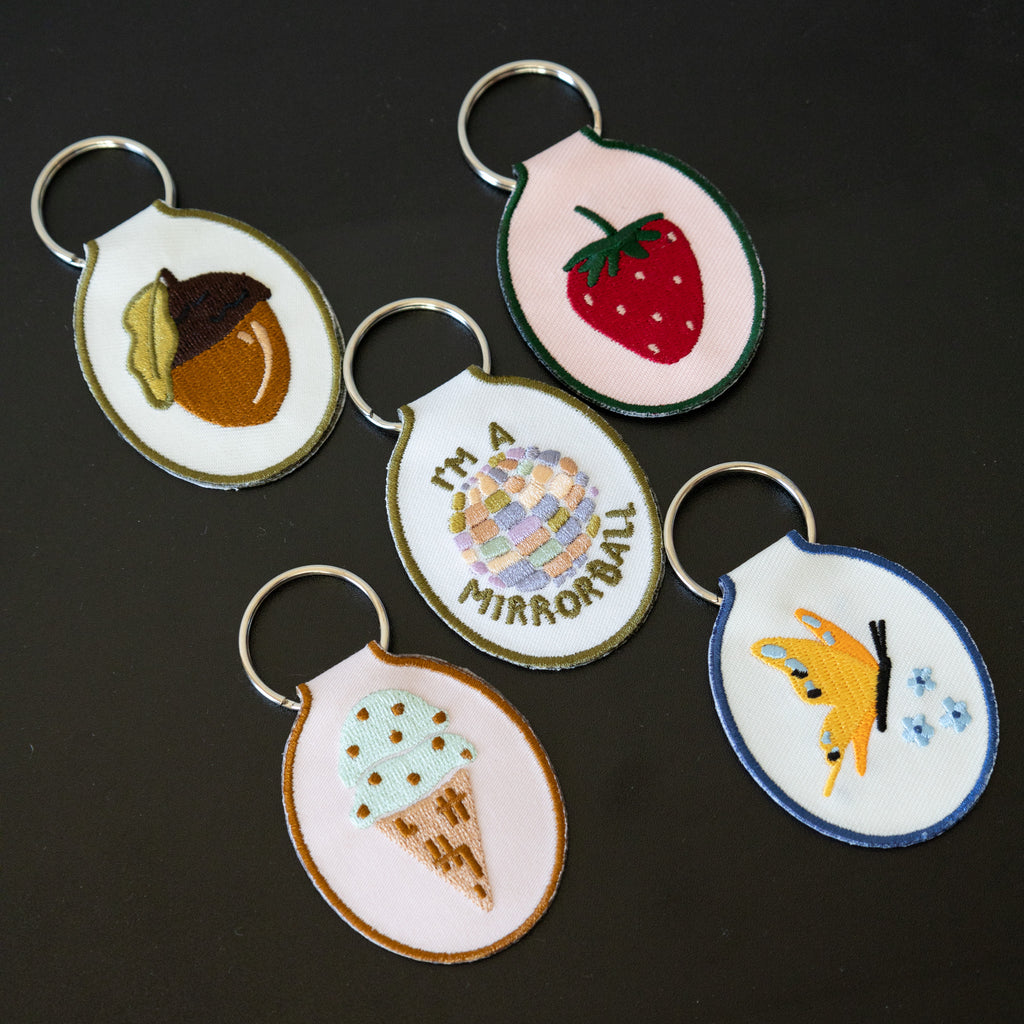 Embroidered keychains with 5 different designs displayed on a black background.