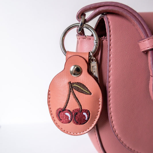 Pink handbag with a keychain featuring cherry design on a white background