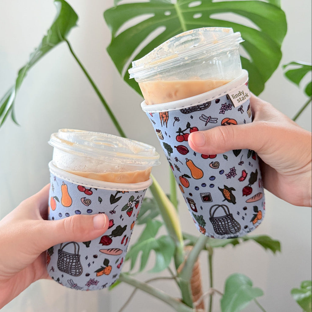 Two hands holding patterned coffee cups with a plant in the background
