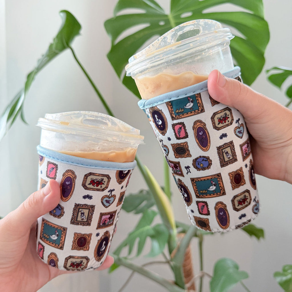 Two hands holding cups with patterned sleeves in front of a plant