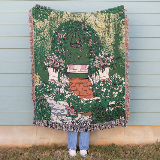 Person holding a decorative blanket with garden design against a light blue wall.