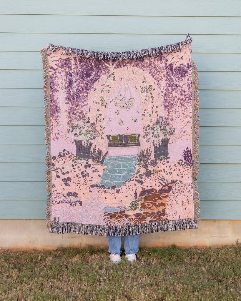 Person holding a decorative blanket with floral and nature patterns against a light blue wall.