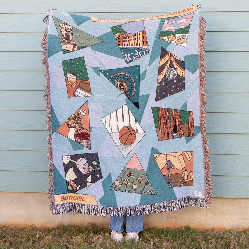 Person holding a colorful quilt with geometric patterns against a light blue wall.