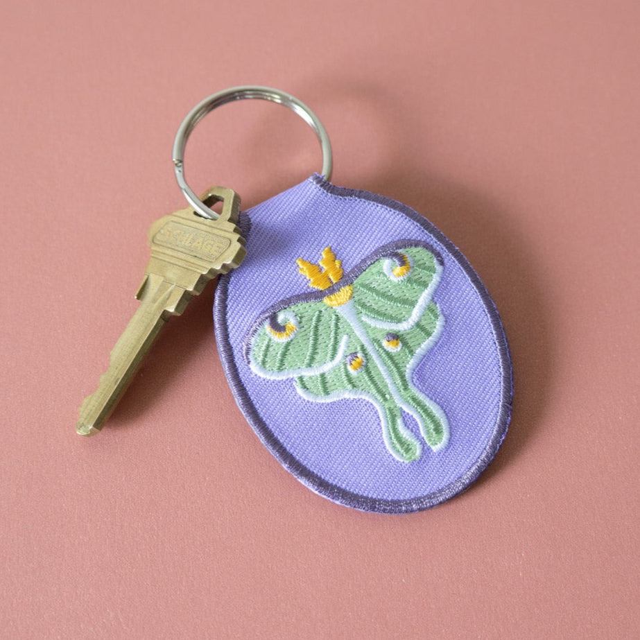 Keychain with embroidered green luna moth design on a purple background