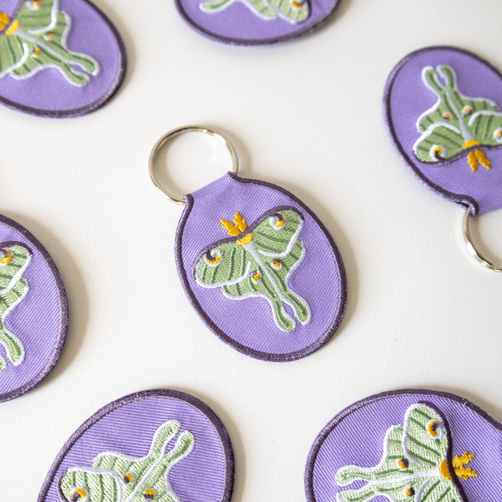 Purple keychains with green luna moth designs on a white background