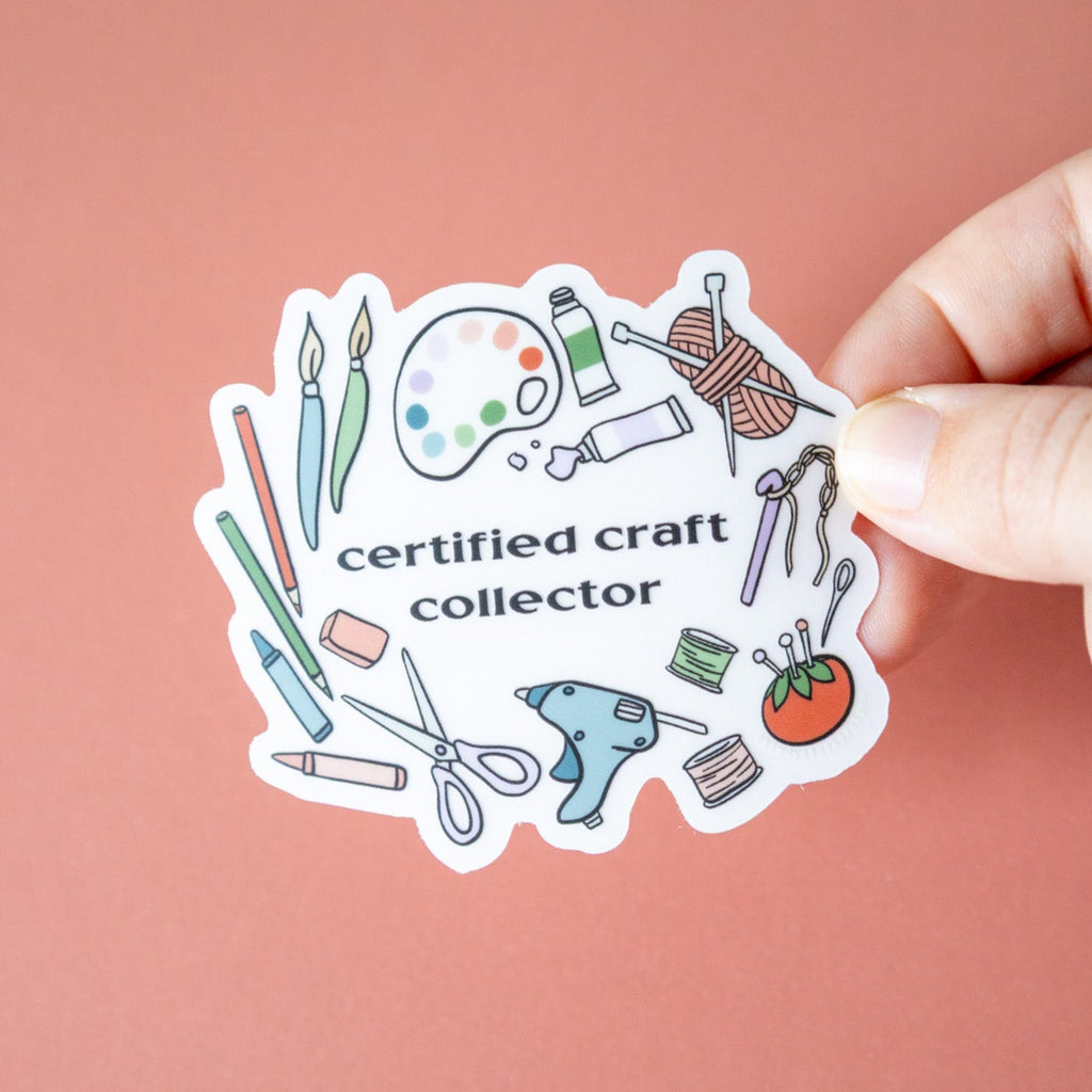 Sticker with craft-related illustrations and text 'certified craft collector' held against a pink background