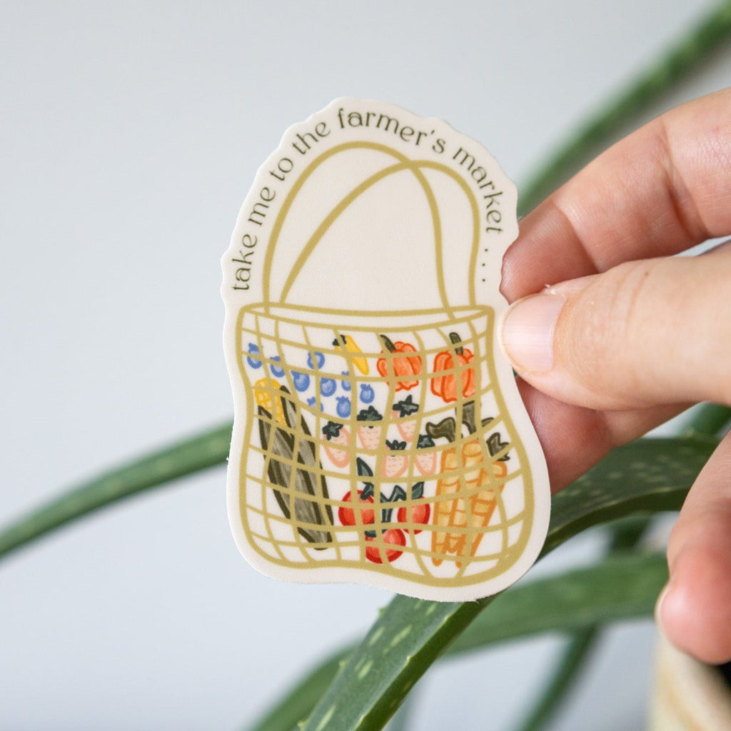 Hand holding a sticker of a basket with vegetables against a light background