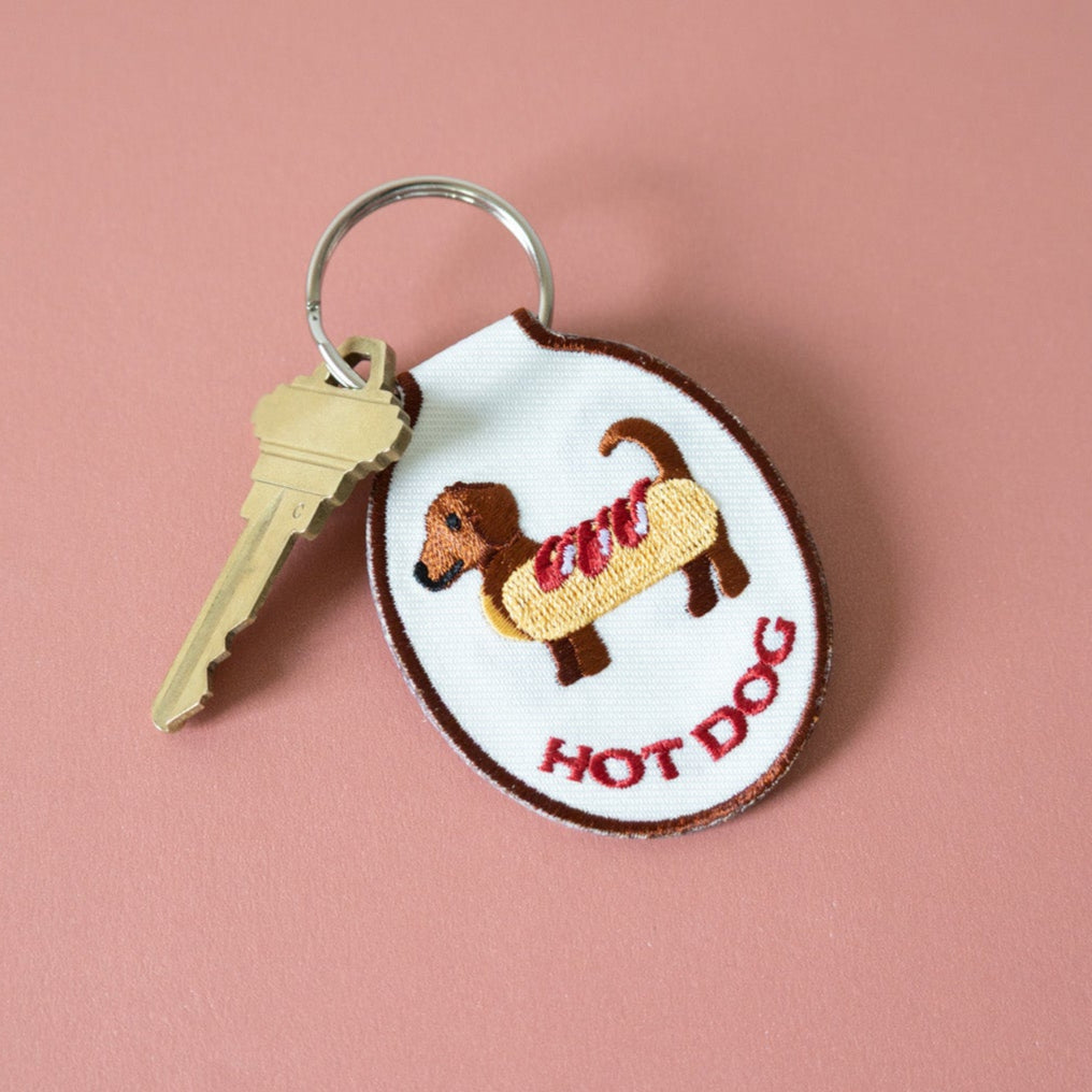 Embroidered keychain with a hot dog dachshund design sitting on a pink background.