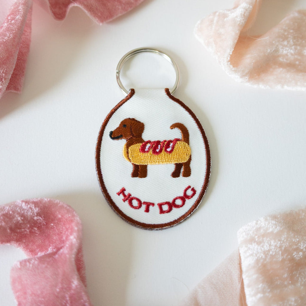 Embroidered keychain of a hot dog dachshund on a white background with pink ribbons.
