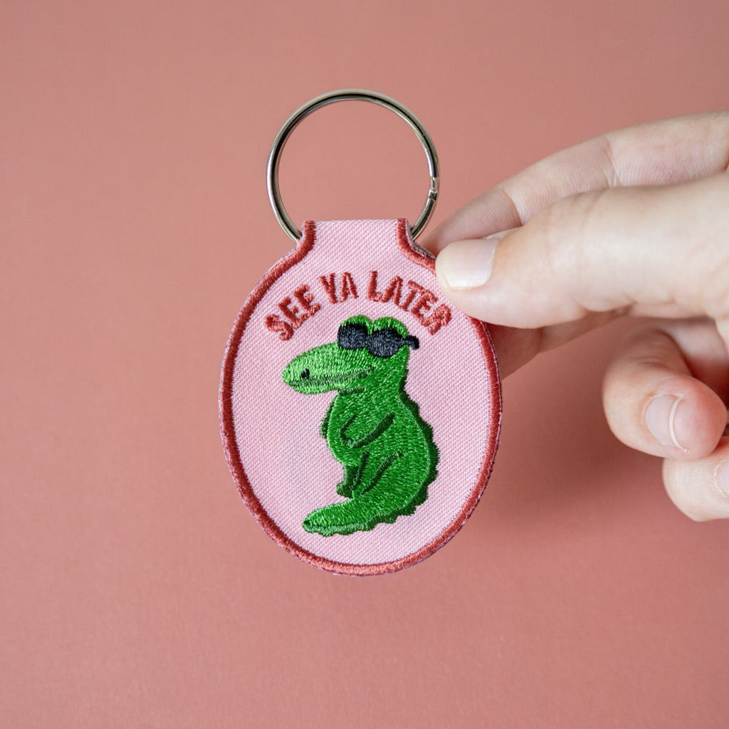 Pink embroidered keychain with green alligator design and 'See Ya Later' text held against a pink background