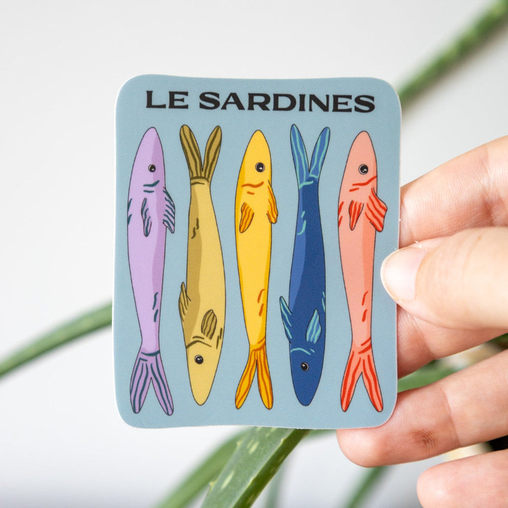 Card with colorful illustrations of sardines held by a hand against a plant background