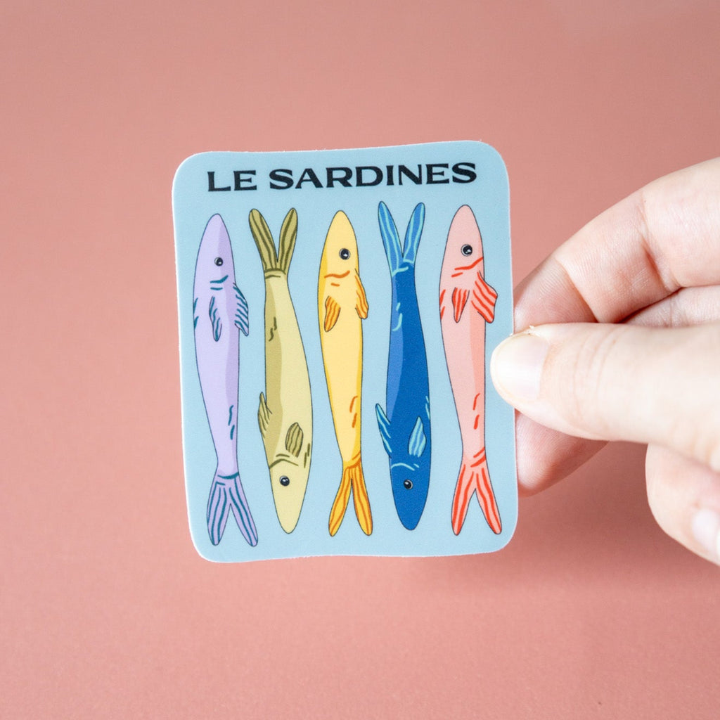 Sticker with illustrations of sardines held by a hand against a pink background