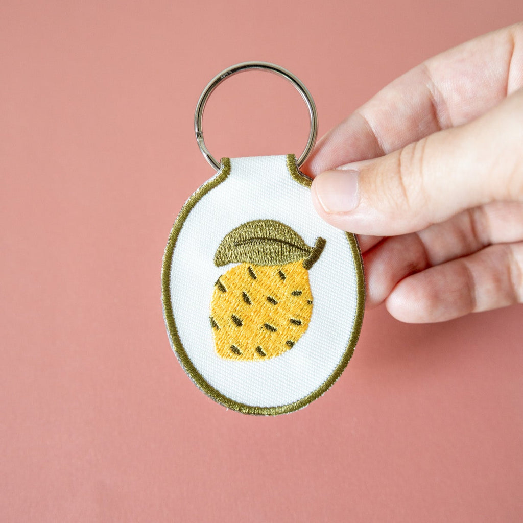 Hand holding a keychain with a lemon design against a pink background