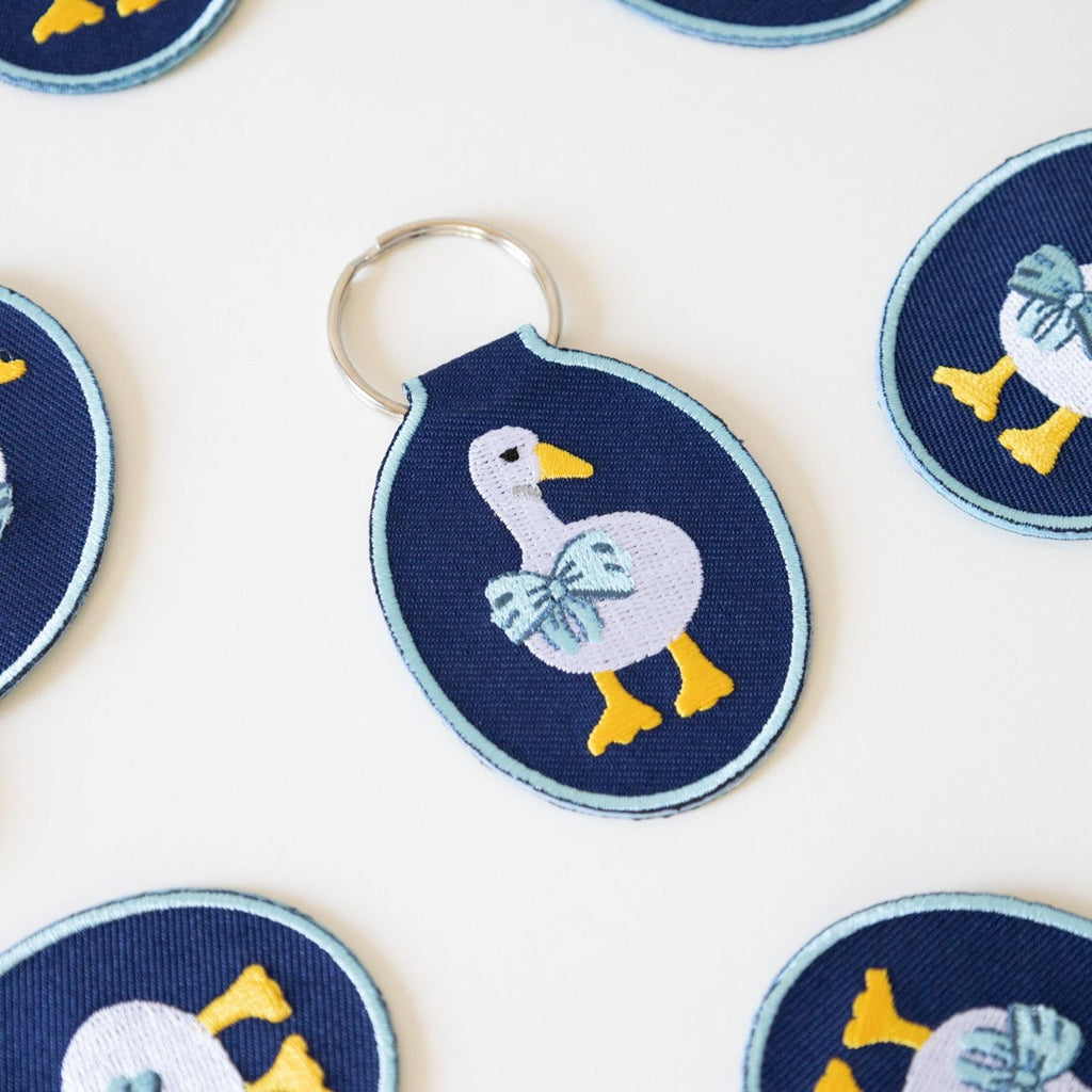 Multiple navy twill keychains with an embroidered duck/goose design, displayed on a white background.
