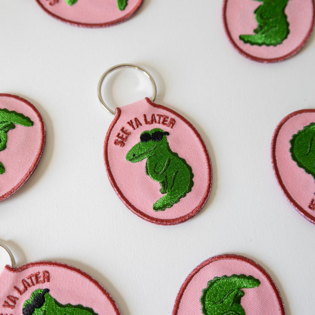Pink embroidered keychains with green alligators and 'See Ya Later' text on a white background