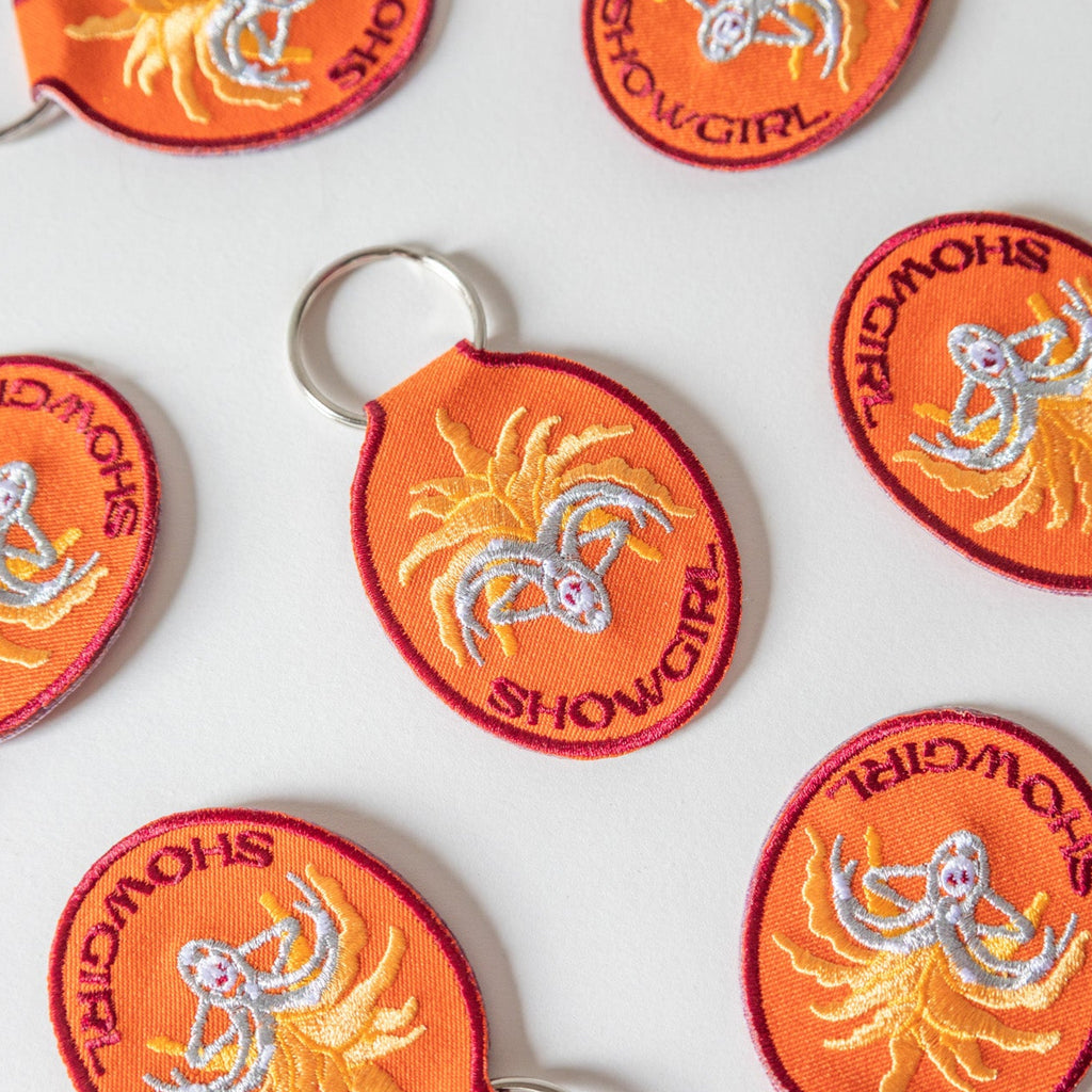 Set of orange and red keychains with 'Showgirl' design on a white 