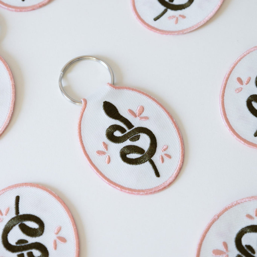 Multiple white cotton twill keychains with an embroidered snake design, displayed on a white background.