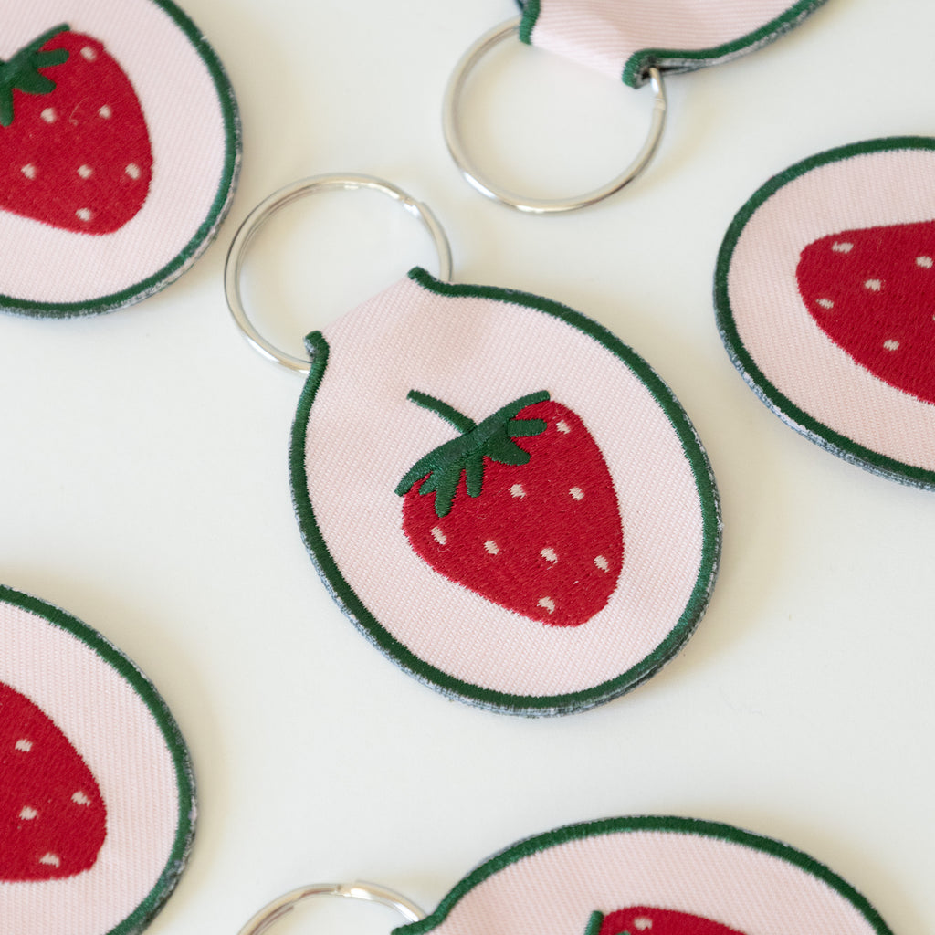 Multiple light pink keychains with an embroidered strawberry design, displayed on a white background.