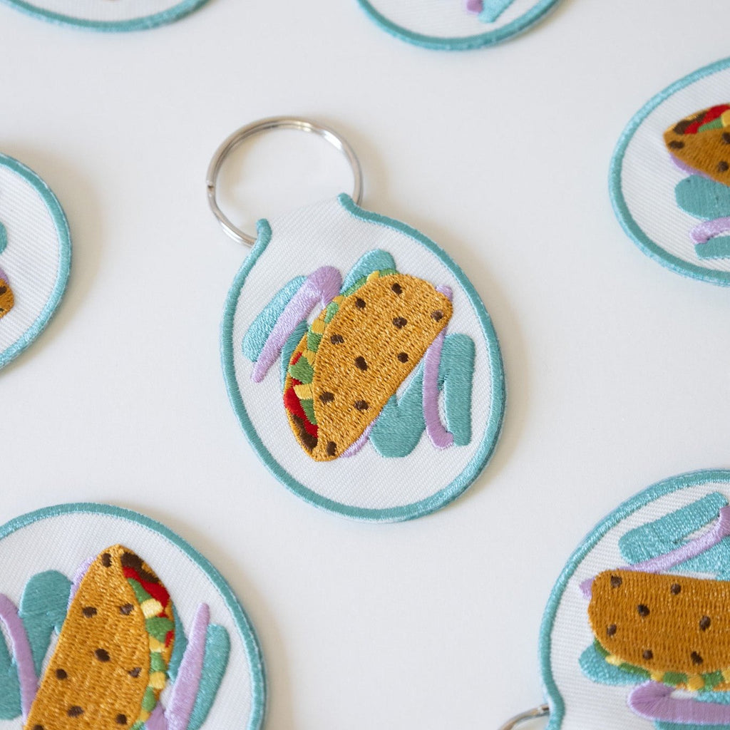 Multiple embroidered keychains with a taco design on white cotton twill, displayed against a white background.