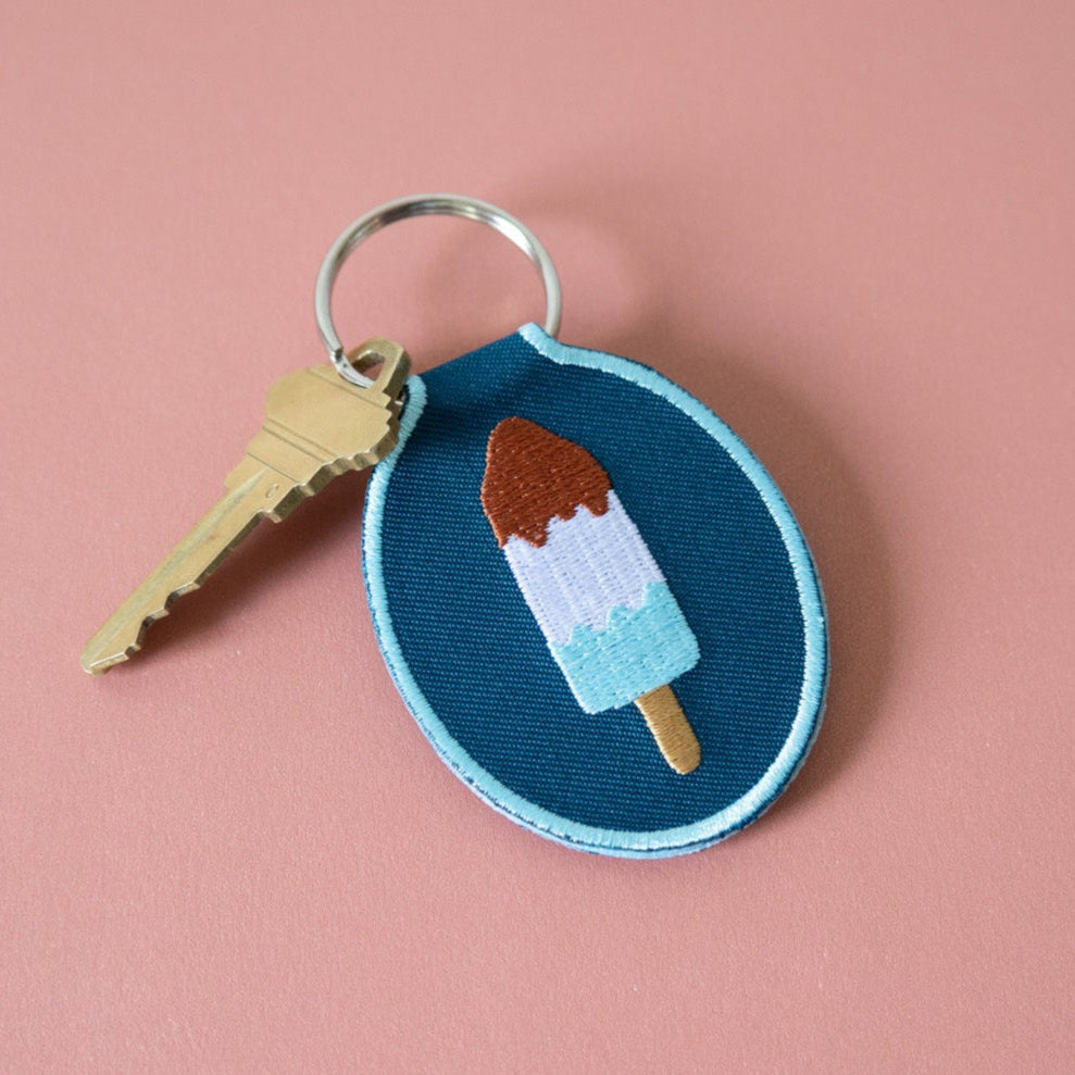 Embroidered keychain with red, white, and blue ice pop design on a blue twill background.