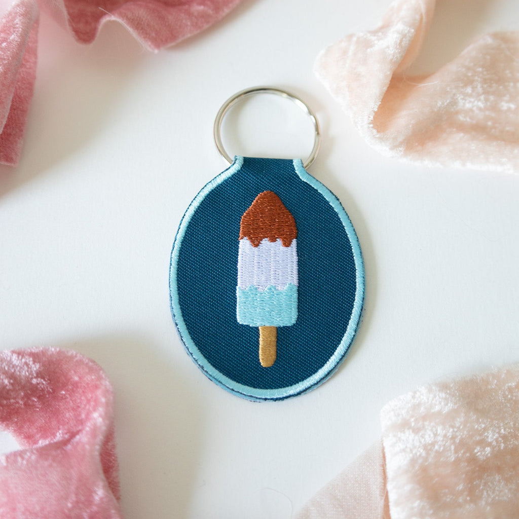 Embroidered keychain with red, white, and blue ice pop design on a soft fabric background.