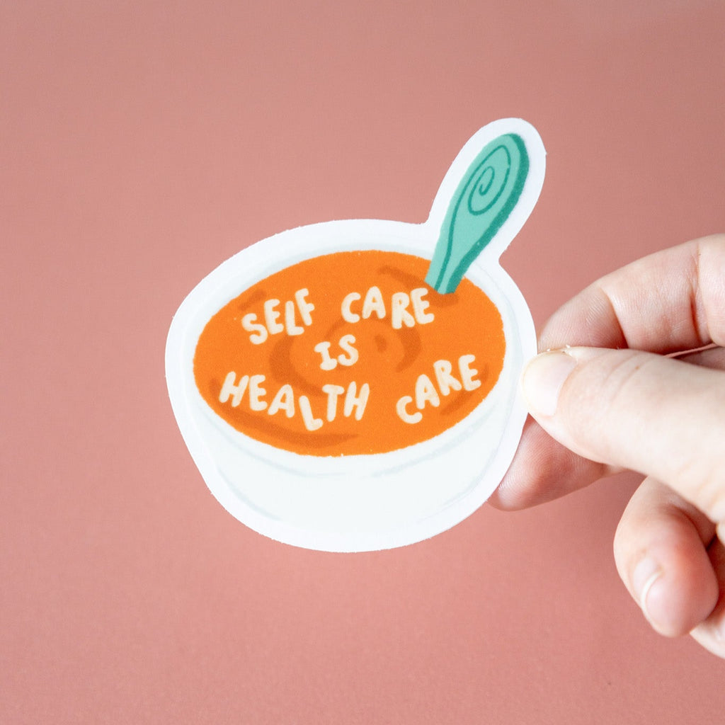 Hand holding a sticker with 'Self care is health care' text on a pink background